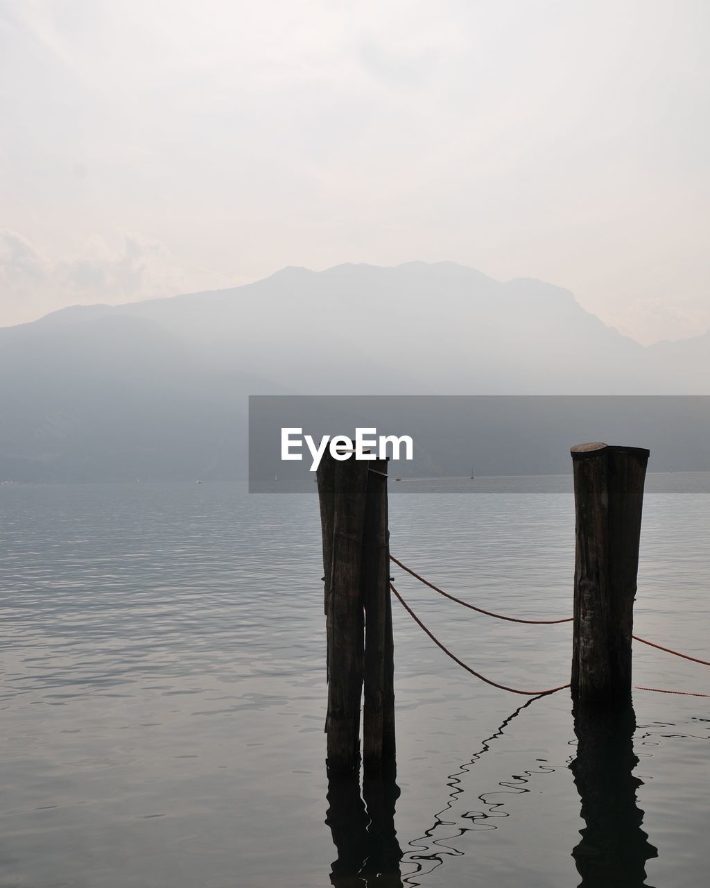 Wooden posts in sea against mountains and sky