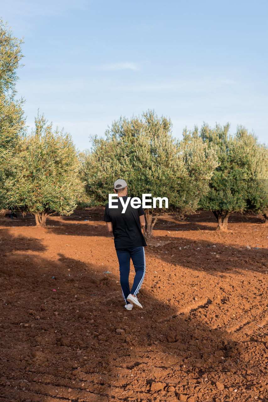 one person, full length, plant, tree, soil, nature, sky, lifestyles, day, field, adult, leisure activity, casual clothing, rear view, agriculture, men, person, land, outdoors, recreation, young adult, sports, dirt, sunlight, motion, landscape, clothing, running