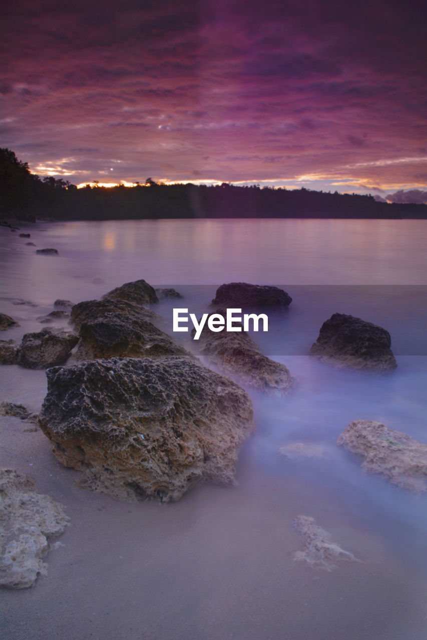 SCENIC VIEW OF ROCKS IN SEA AGAINST SKY DURING SUNSET