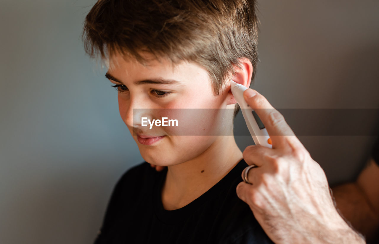 Tween boy getting temperature taken with an ear thermometer.