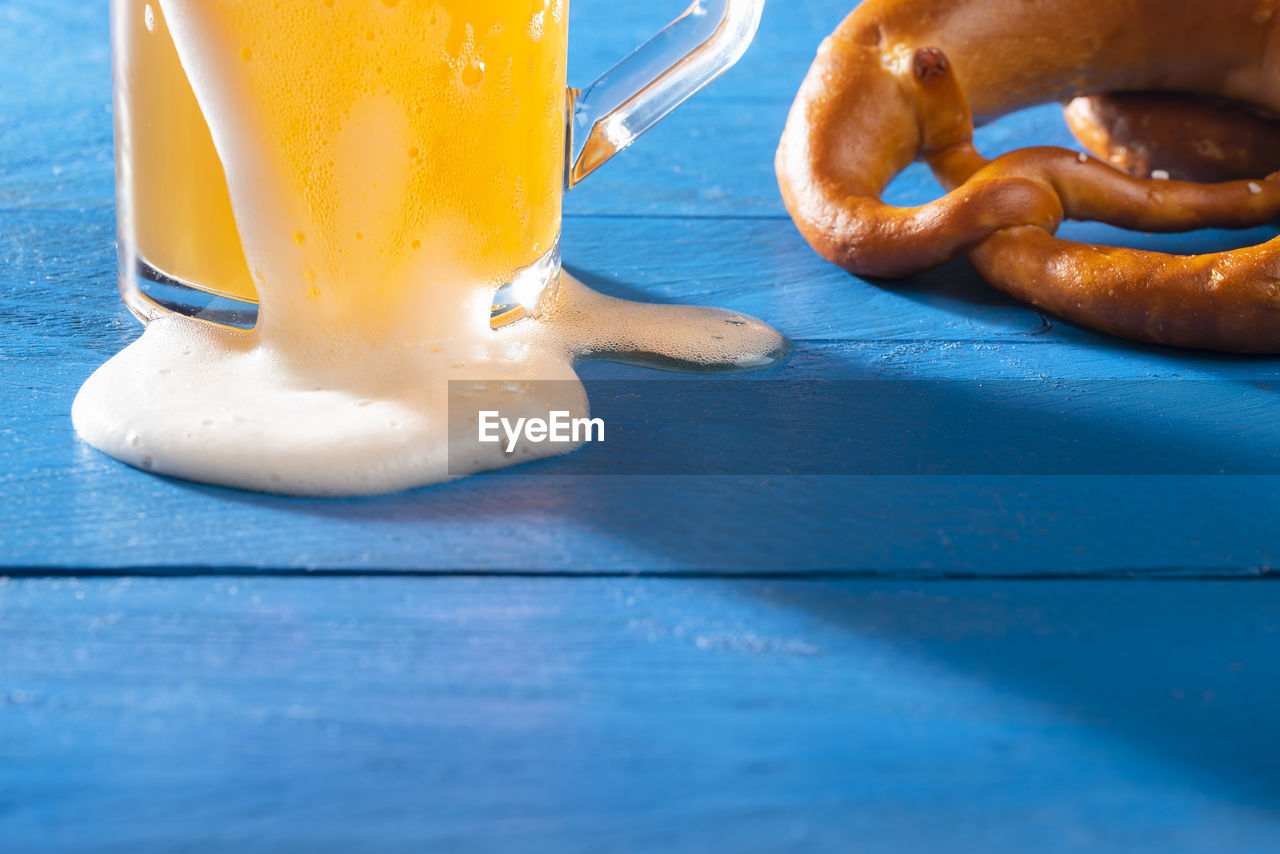 Close-up with a pint of beer with froth and a german pretzel on a blue table. unfiltered beer.