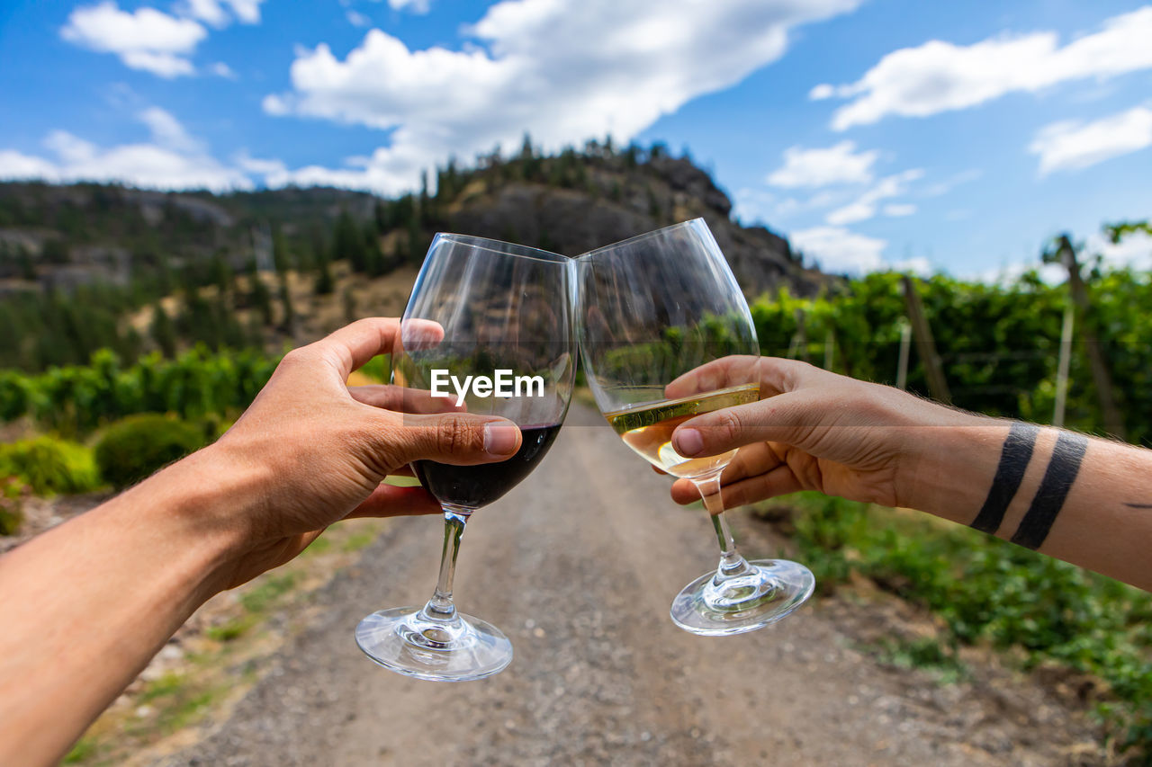 Cropped hands of couple holding wineglass against sky