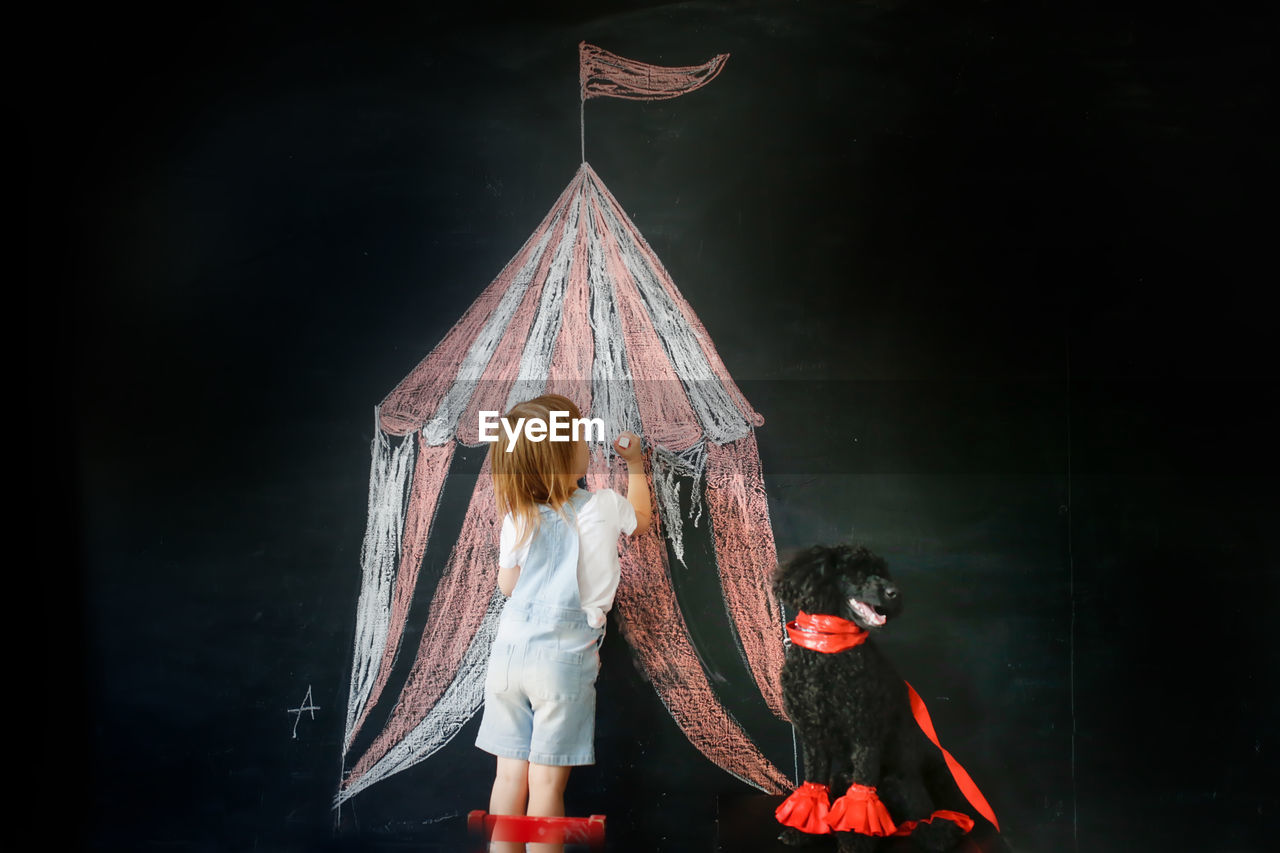 Cute child girl and black poodle dog playing circus. tent drawn in chalk, dog training