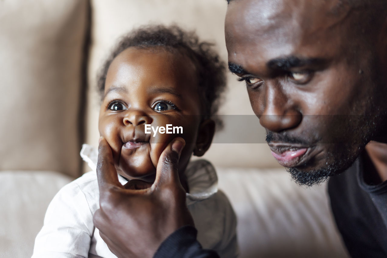 Playful father squeezing baby girl's cheeks at home