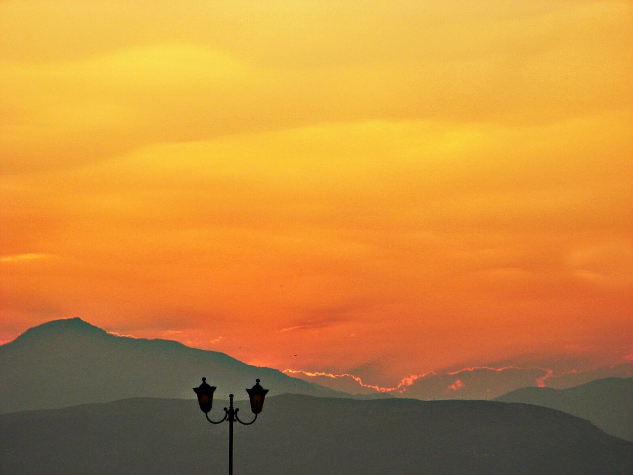 Silhouette street light with mountains against orange sunset sky