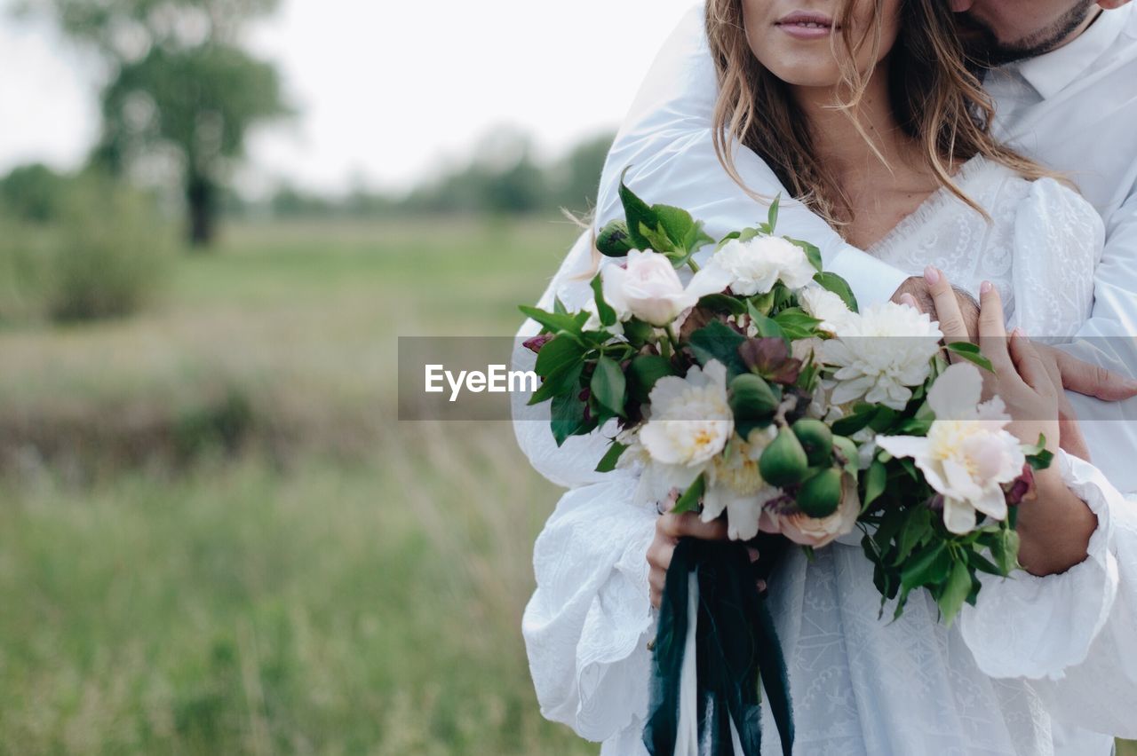 Cropped image of bridegroom embracing bride standing on field