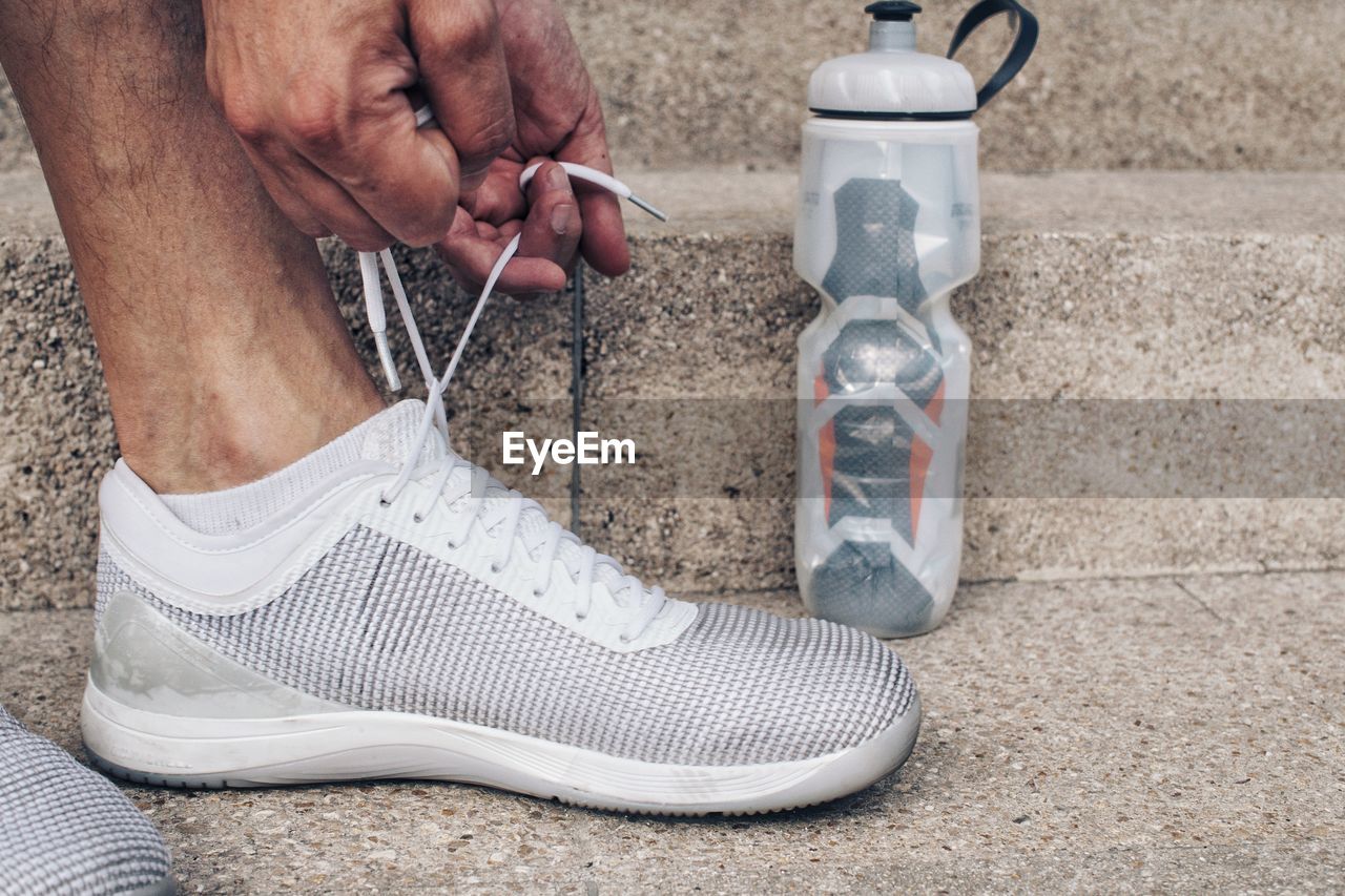 Low section of man tying shoe by water bottle on steps