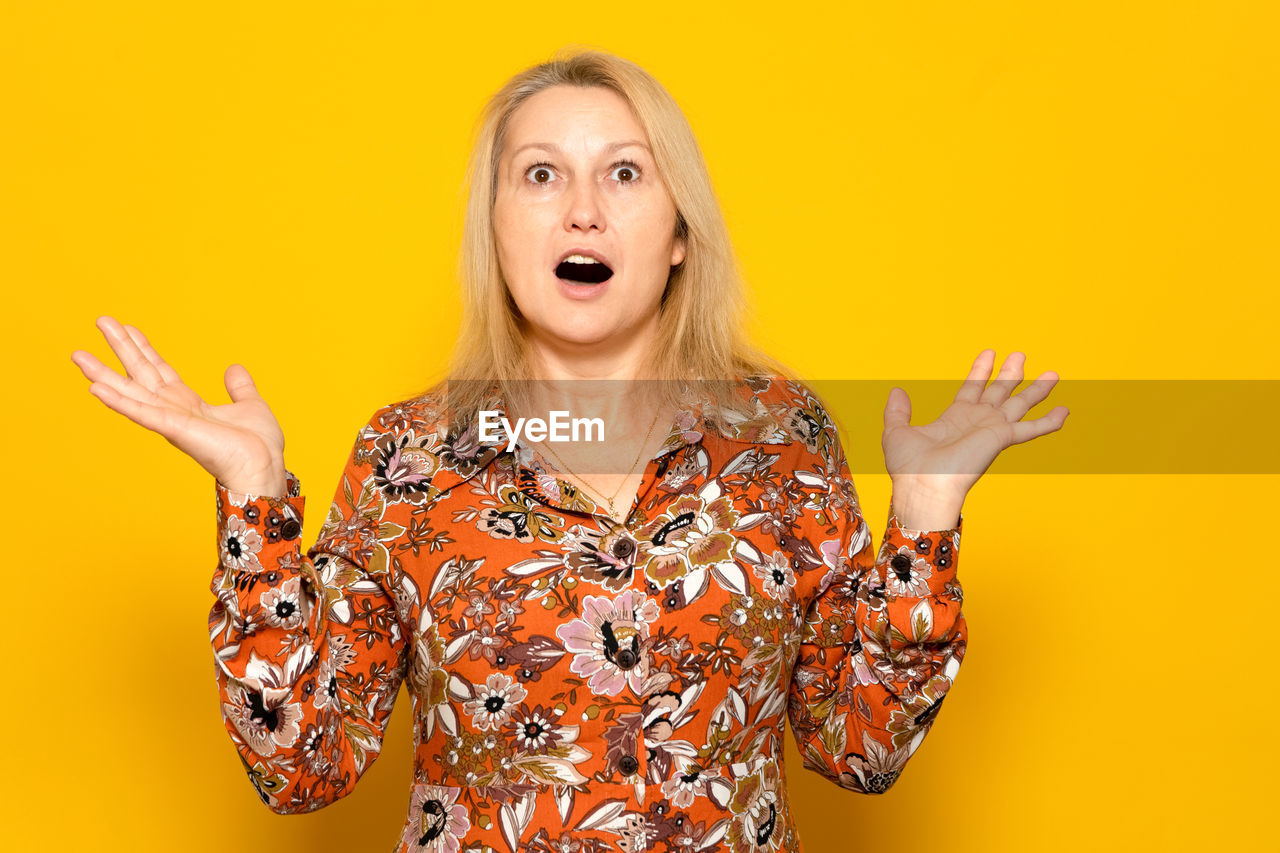 studio shot, yellow, blond hair, colored background, one person, portrait, women, adult, mouth open, emotion, indoors, shouting, young adult, looking at camera, yellow background, gesturing, waist up, hairstyle, fun, facial expression, human mouth, anger, surprise, person, fashion, front view, female, arm, long hair, positive emotion, copy space, excitement, negative emotion, sign language, finger, humor, happiness, limb