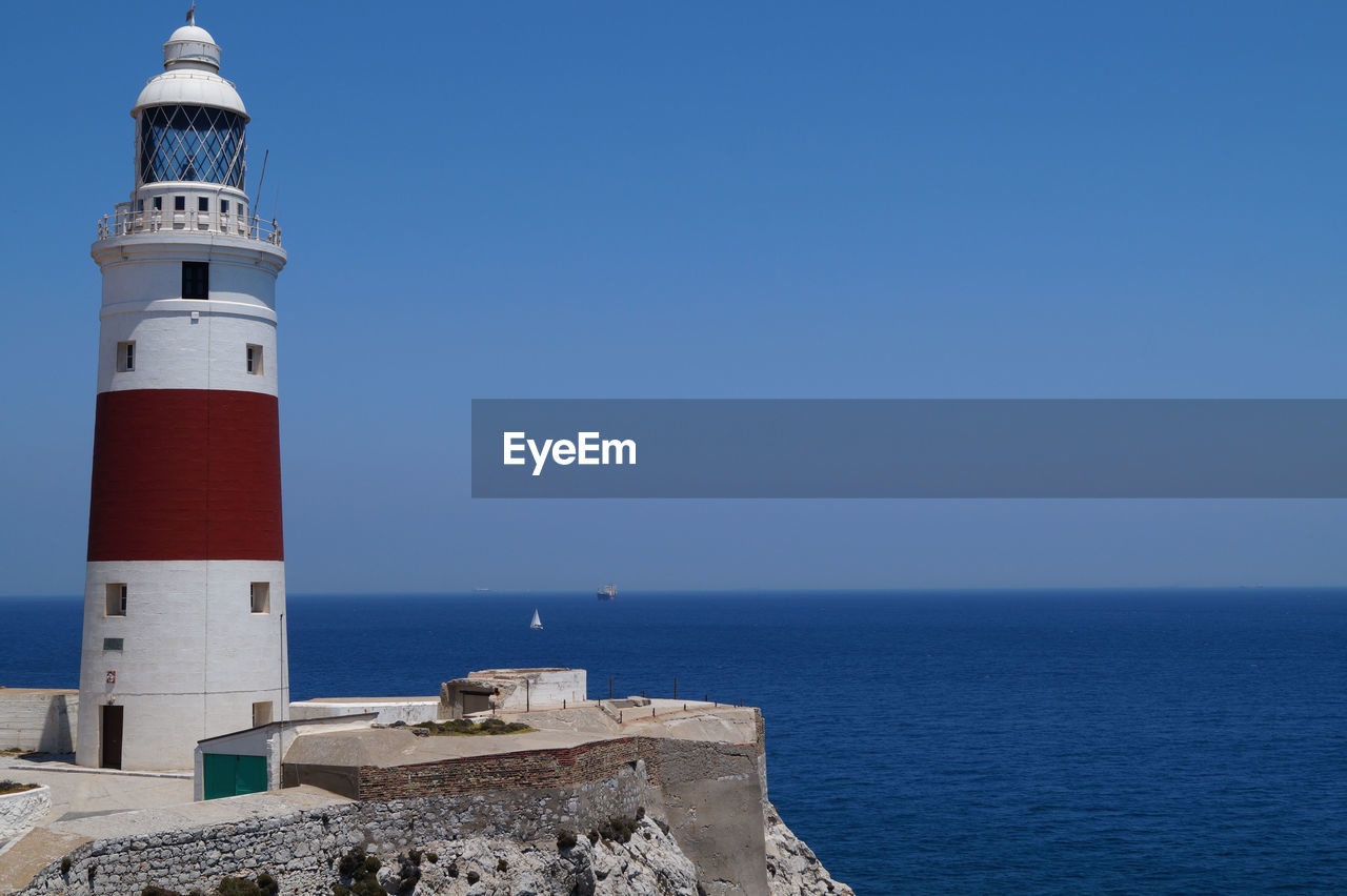 Lighthouse by sea against clear sky