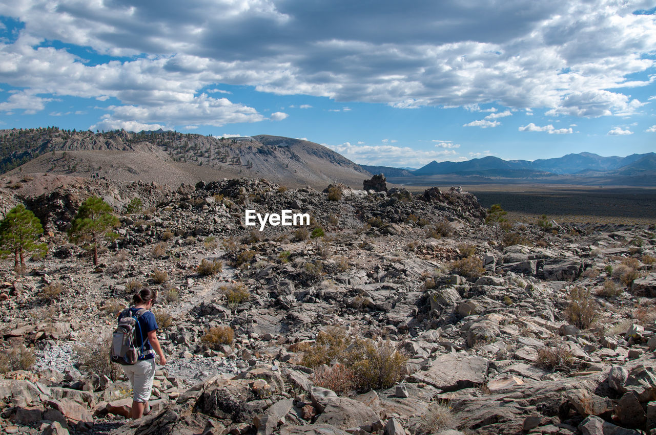 Woman walking on rocks against sky in sunny day