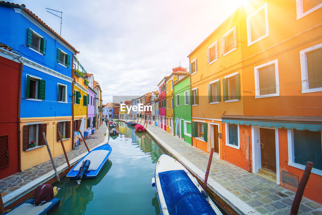 architecture, water, building exterior, nautical vessel, built structure, canal, travel destinations, nature, transportation, sky, travel, city, tourism, multi colored, building, mode of transportation, window, gondola, residential district, trip, vacation, waterway, sunlight, holiday, cloud, reflection, vehicle, outdoors, town, house, tranquility, boat, day, beauty in nature, idyllic, sea, in a row, summer, tranquil scene, moored, no people, blue, sunny, diminishing perspective