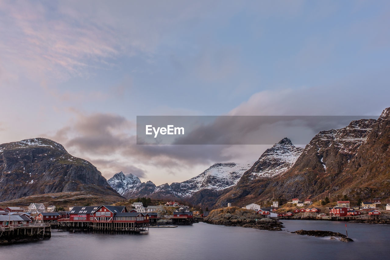 Buildings by sea and mountains against sky