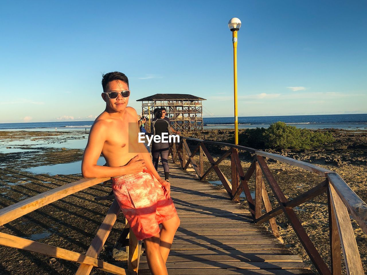 Portrait of shirtless man standing on footbridge at beach