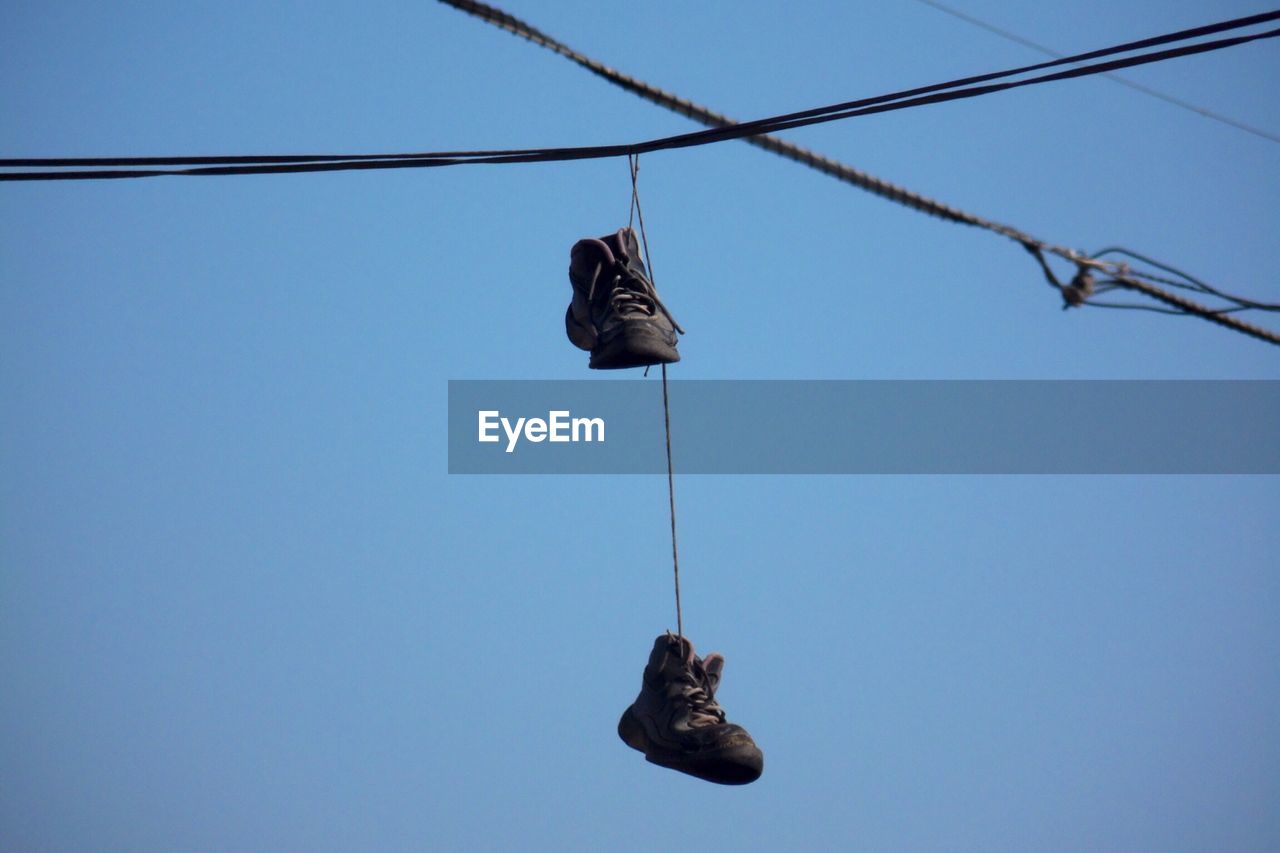 Shoes hanging on cable against clear sky