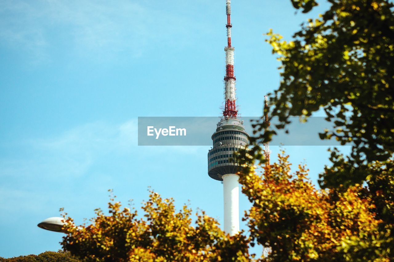 Low angle view of trees by communication tower against sky