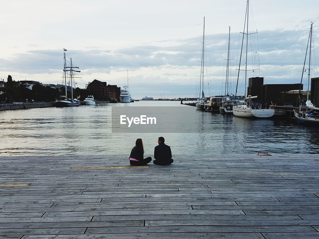 PEOPLE SITTING ON MOORED AT SEA AGAINST SKY