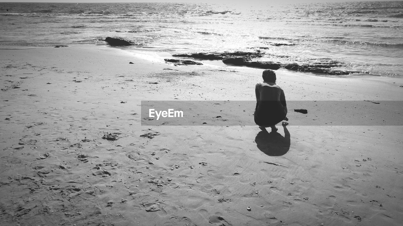 Rear view of young woman crouching at beach