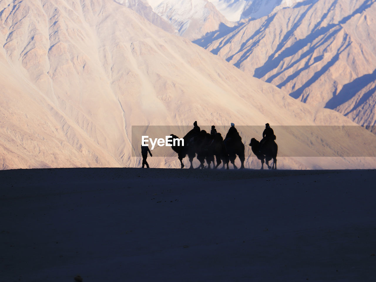 People riding camels on sand against mountains