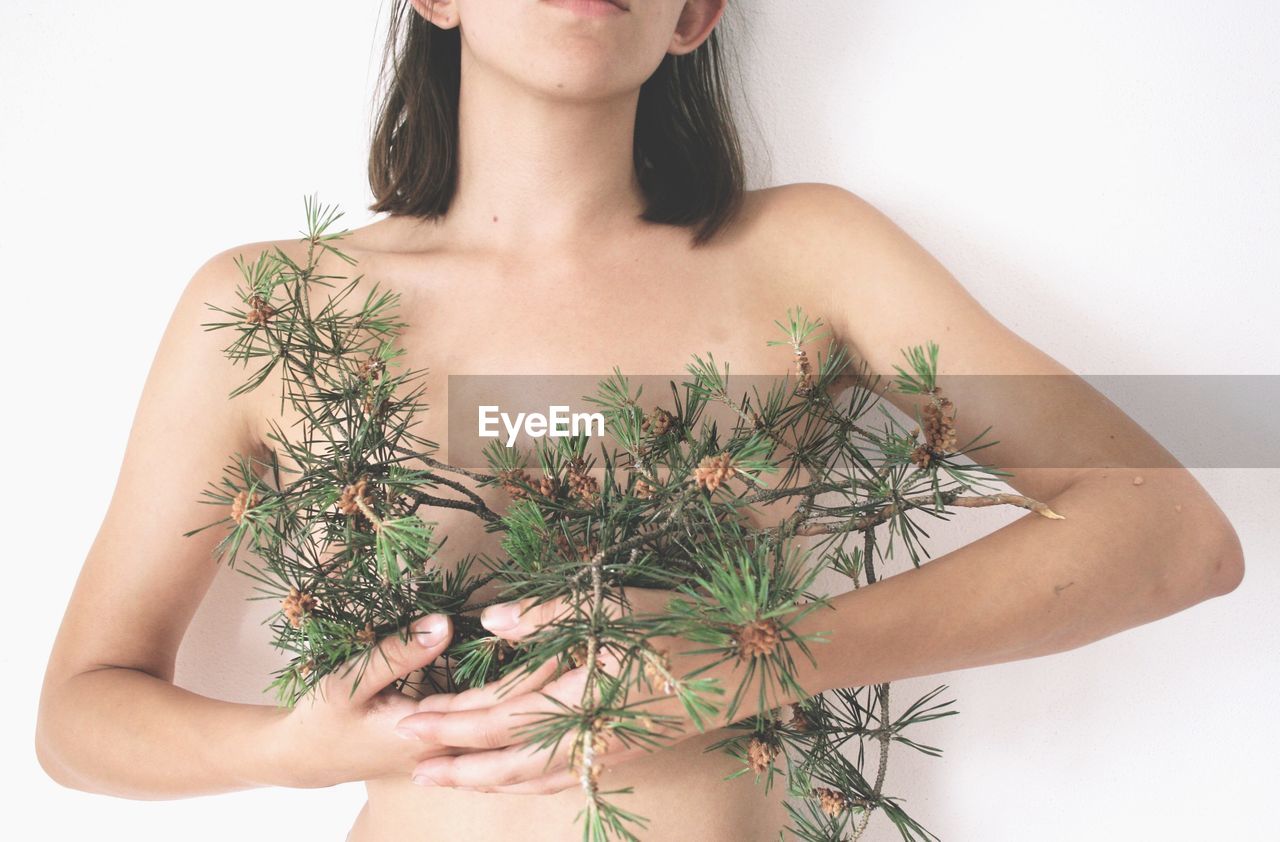 Midsection of shirtless young woman standing against white background