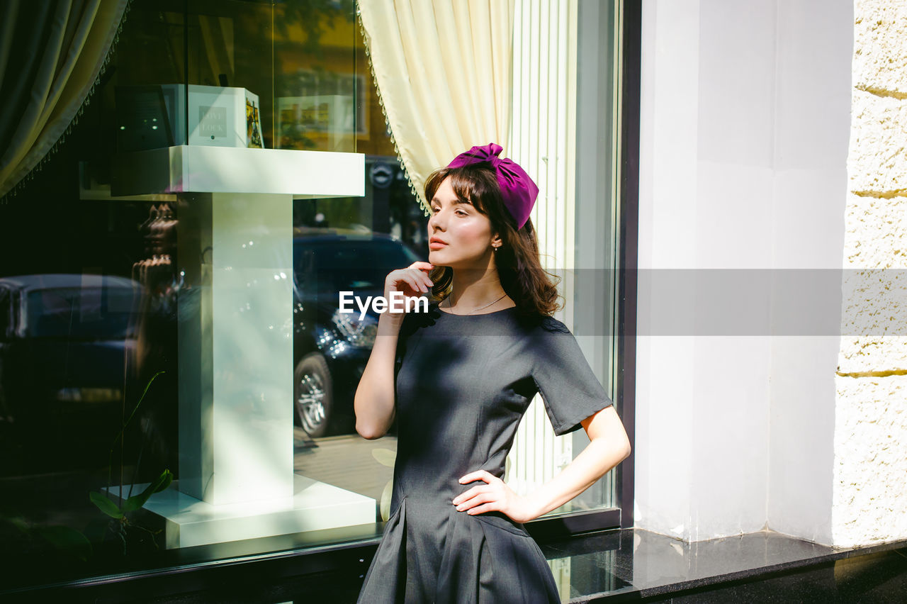 Beautiful young woman in black dress standing by building