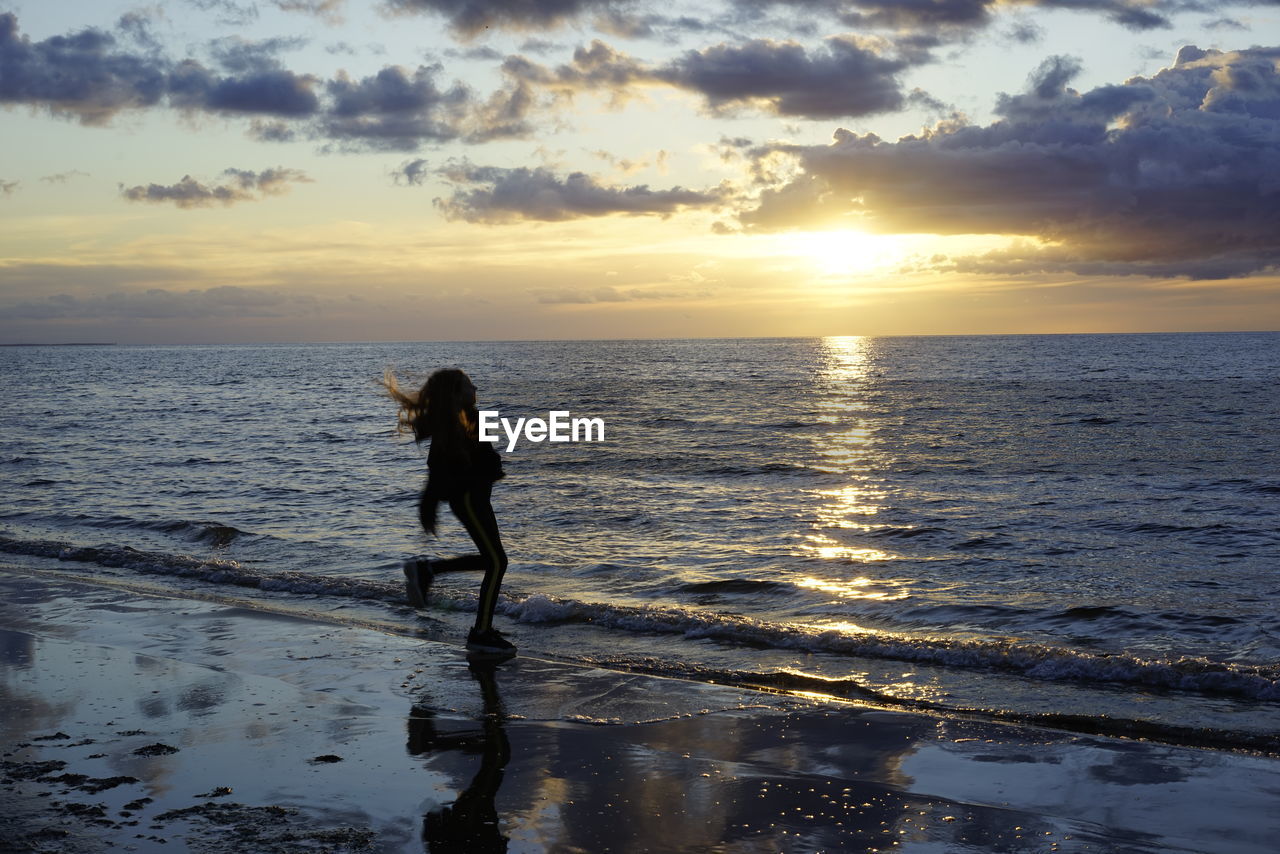 MAN STANDING AT BEACH DURING SUNSET