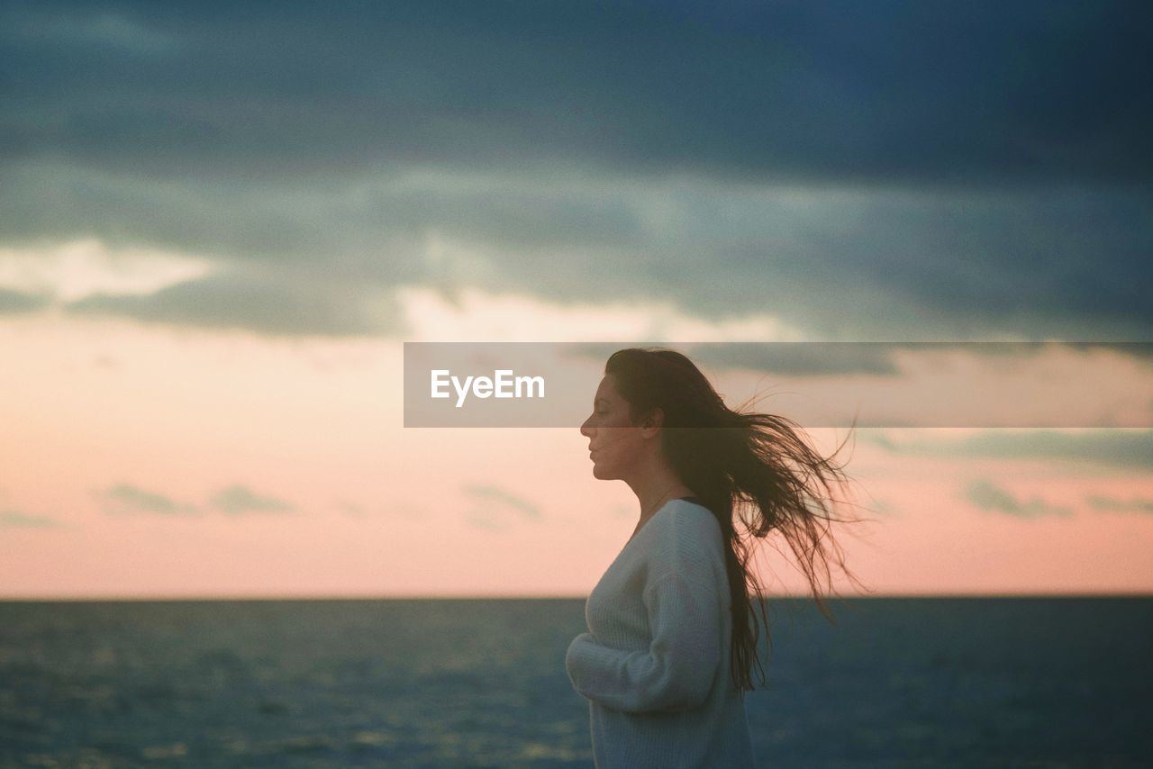 Side view of woman standing against sea during sunset