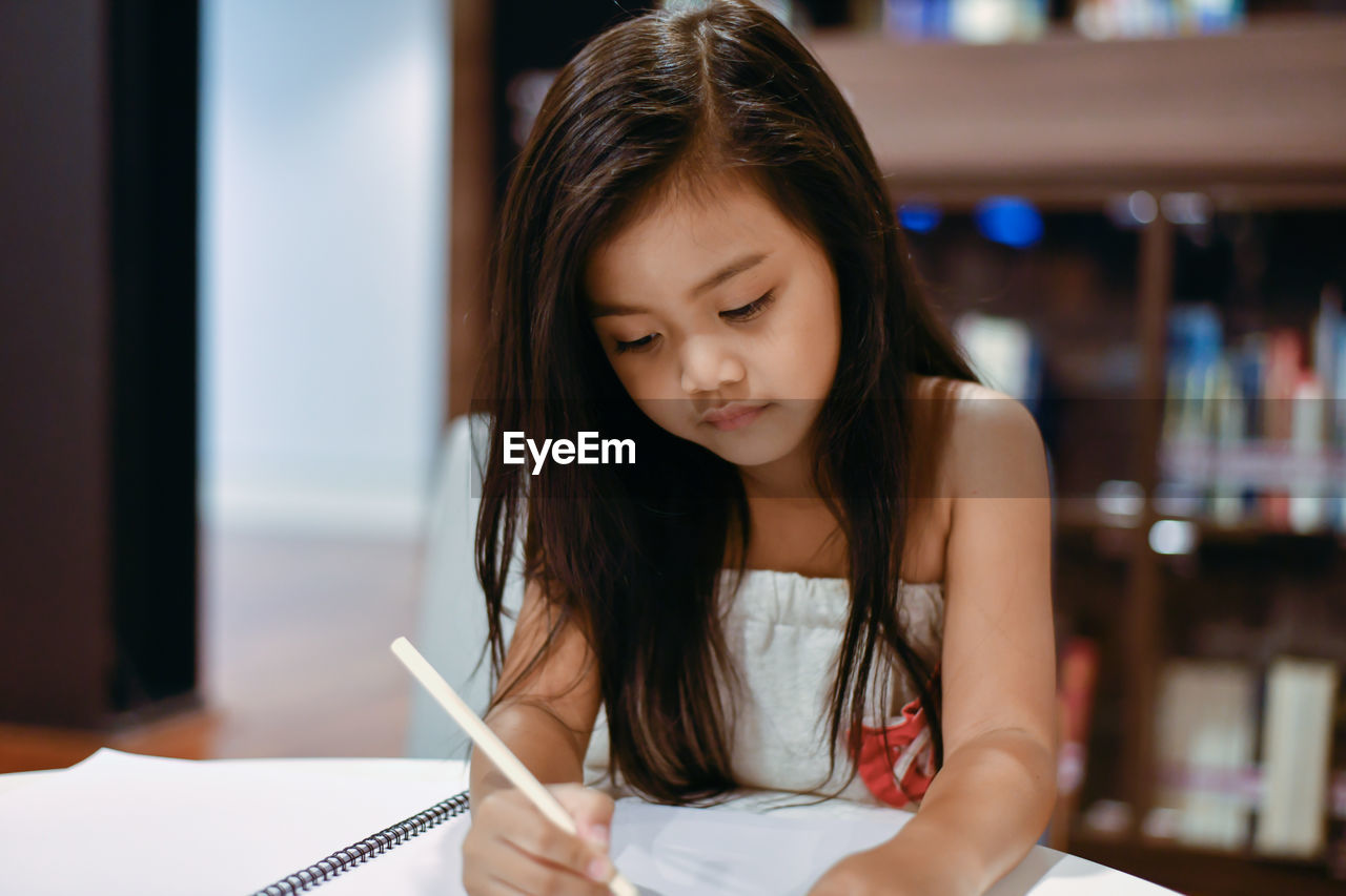 Girl writing while sitting on table