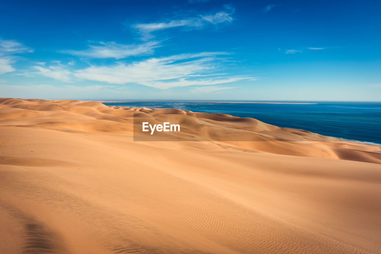 Scenic view of sand dunes by sea against blue sky