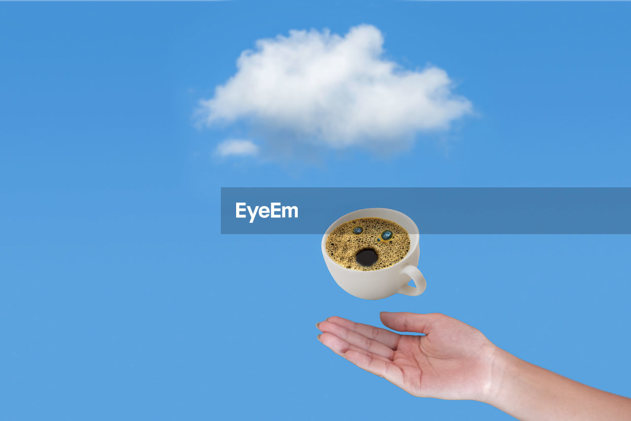 Hand of woman holding coffee cup cloudy blue sky