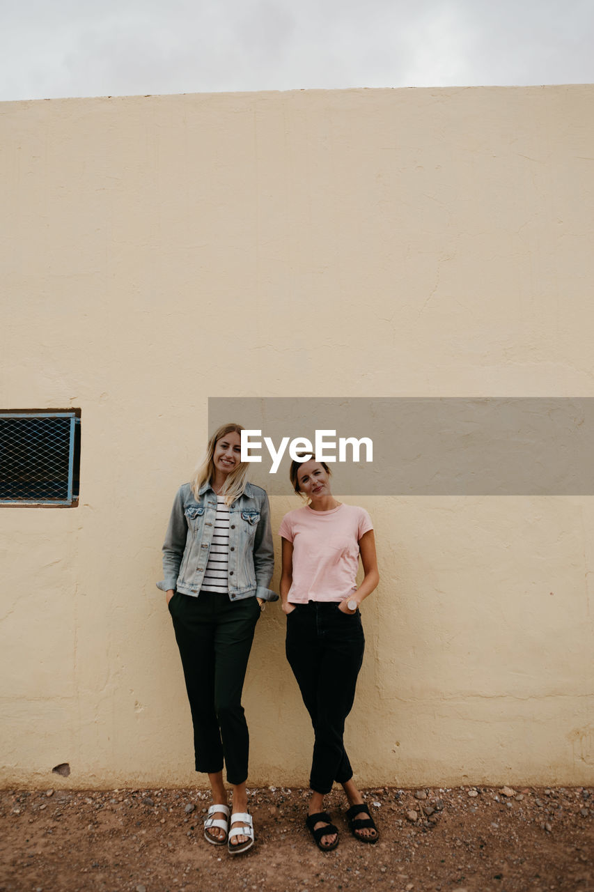 Full length portrait of smiling friends standing against wall