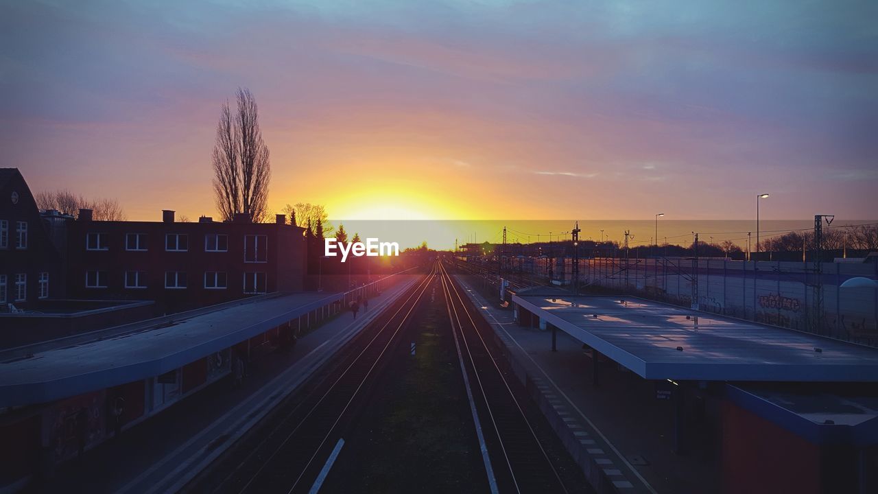 Railroad tracks in city against sky during sunset