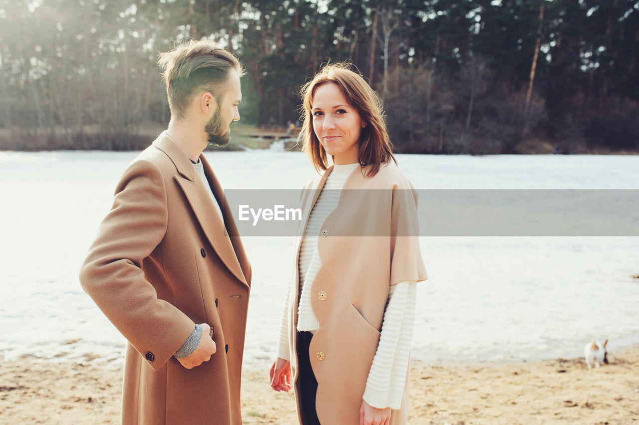 Portrait of smiling young woman standing by boyfriend at riverbank