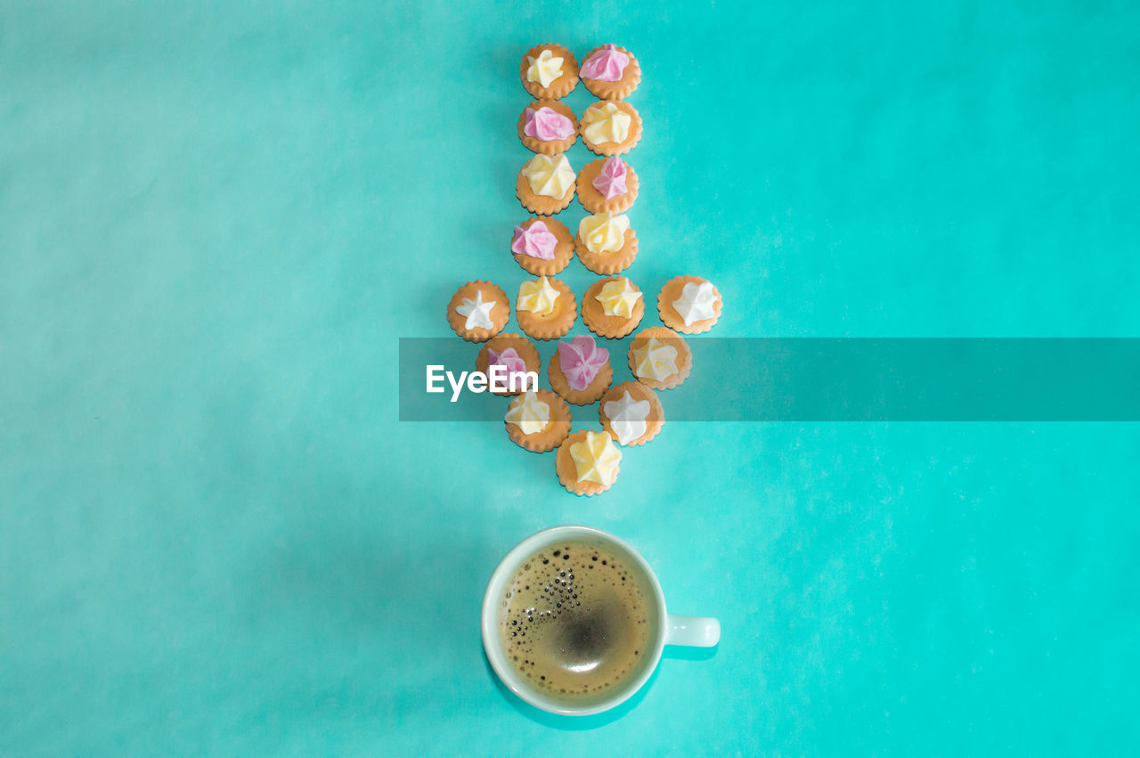 Directly above shot of arrow shaped cookies by black coffee on blue table