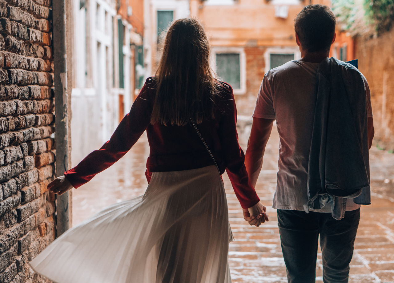 Rear view of couple holding hands while walking on footpath