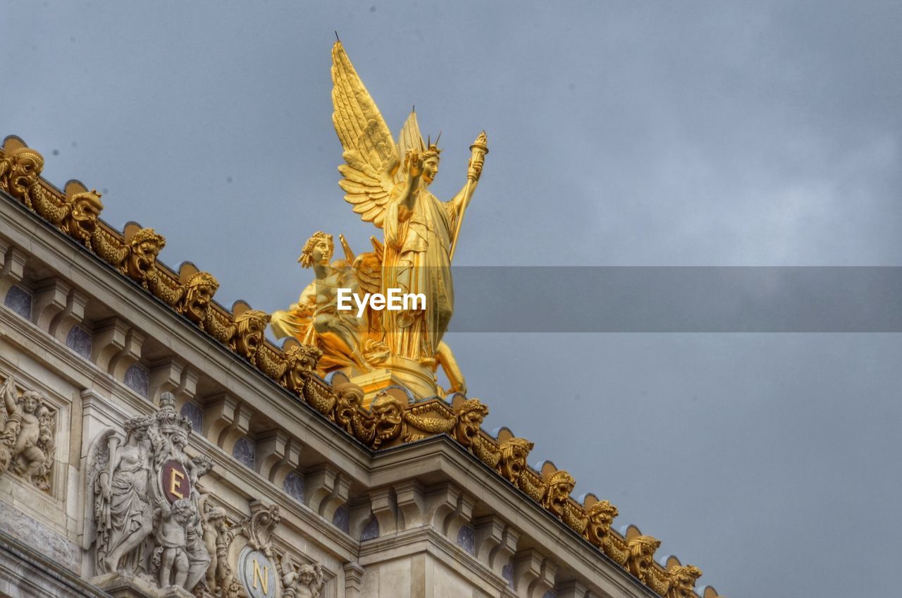 Low angle view of angel statue on building against cloudy sky