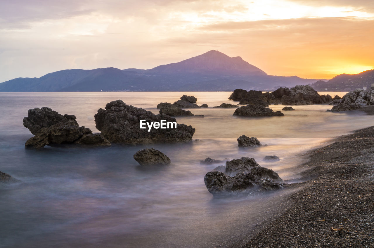 Rocks in sea against sky during sunset