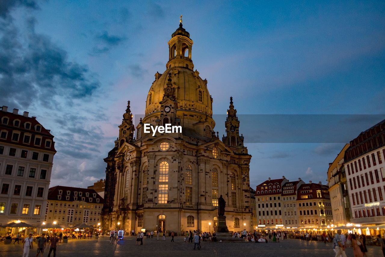 People walking by cathedral and buildings against sky in city