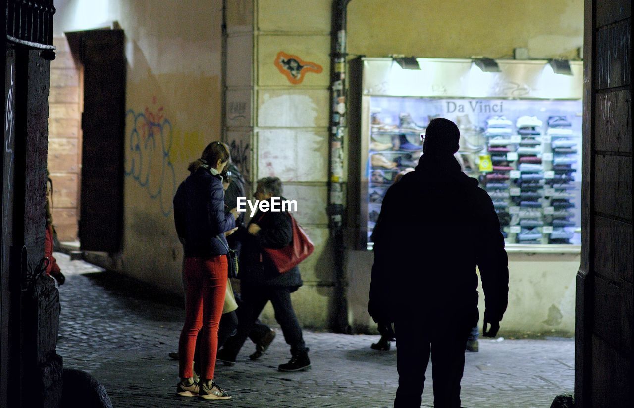 REAR VIEW OF PEOPLE WALKING ON STREET AMIDST BUILDINGS