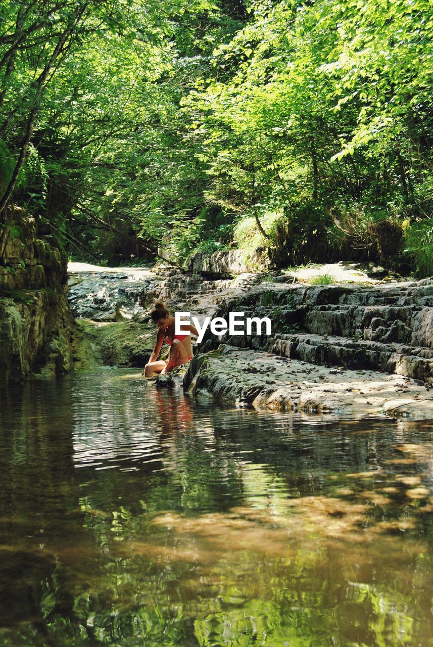 Woman sitting at rock by river in forest