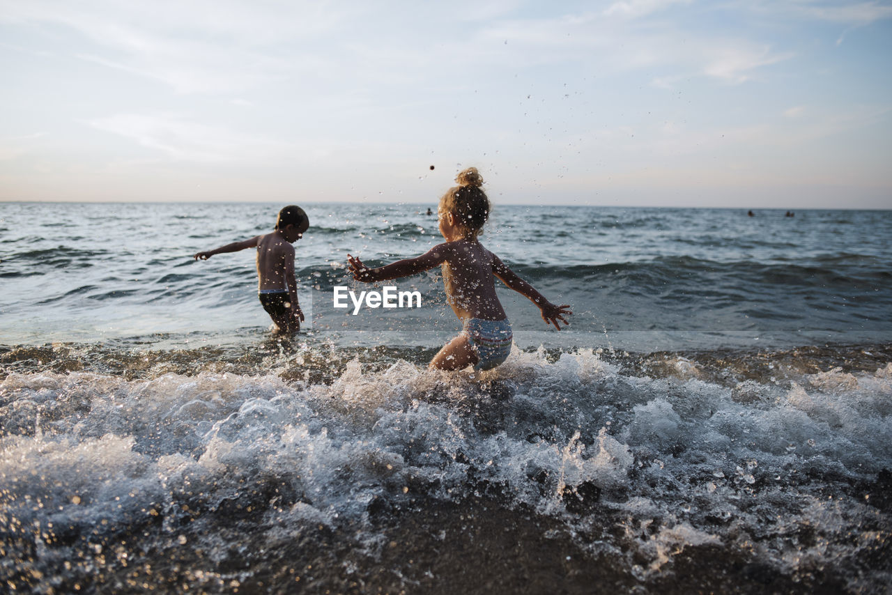 Playful siblings playing in waves at lake simcoe against sky