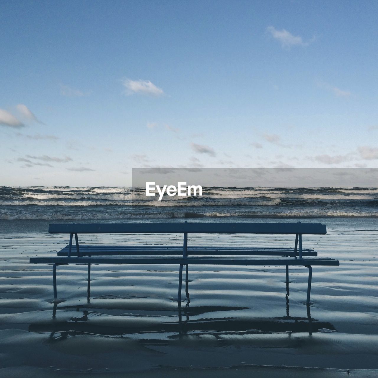 Empty bench at calm beach against sky