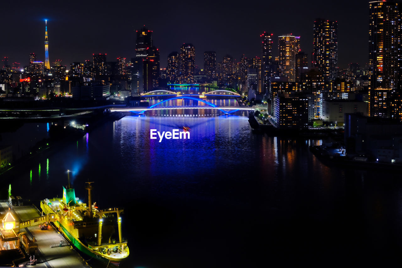 Illuminated tokyo by river against sky at night