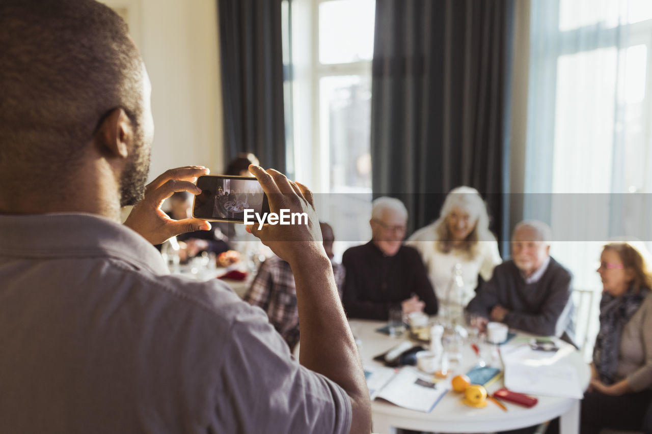 Male caregiver photographing senior men and women on smart phone in nursing home