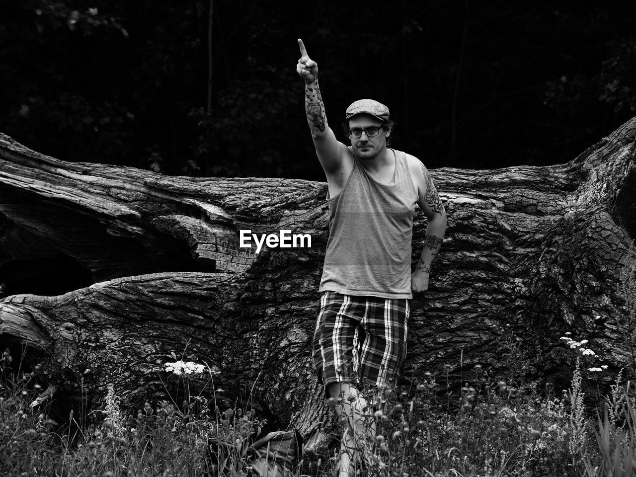 Hipster with hand raised while standing against log in forest