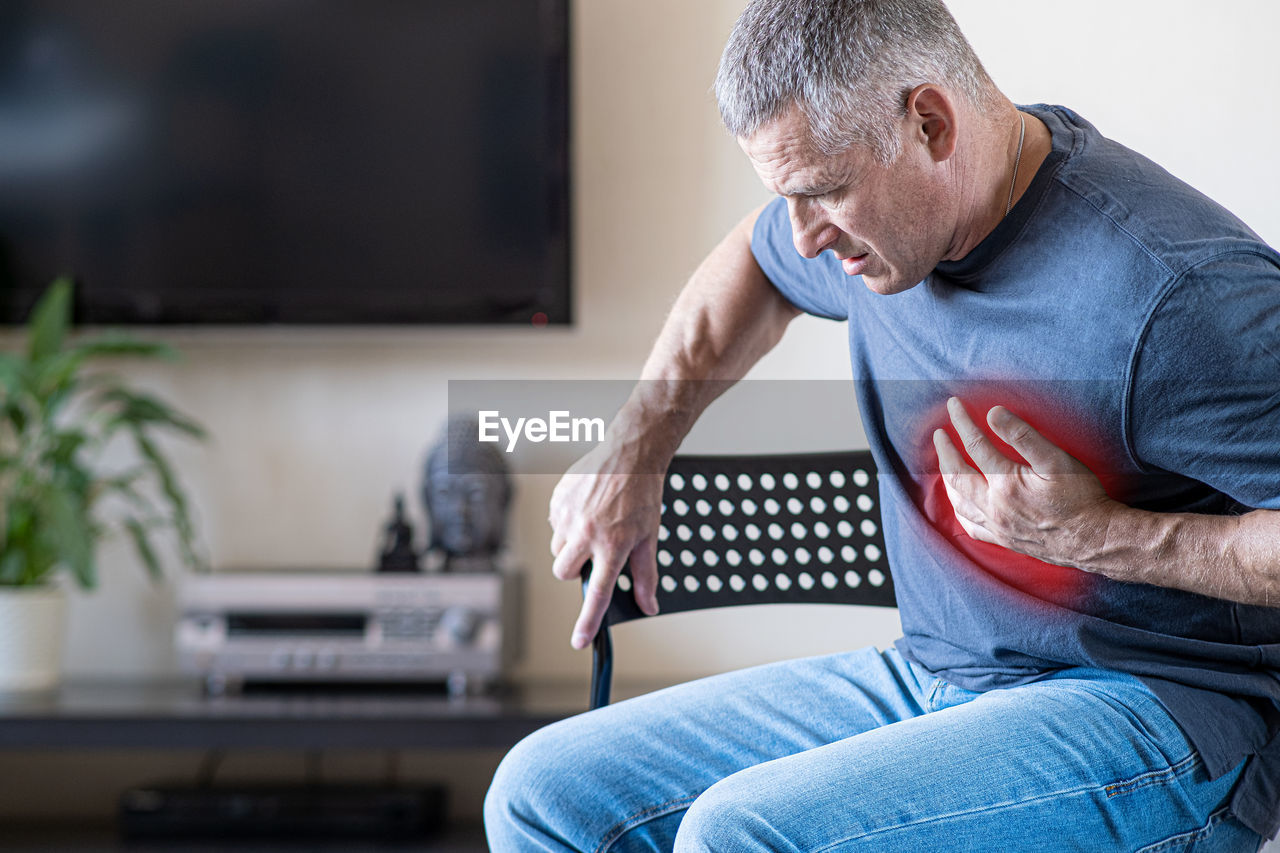 MIDSECTION OF MAN HOLDING MOBILE AT HOME