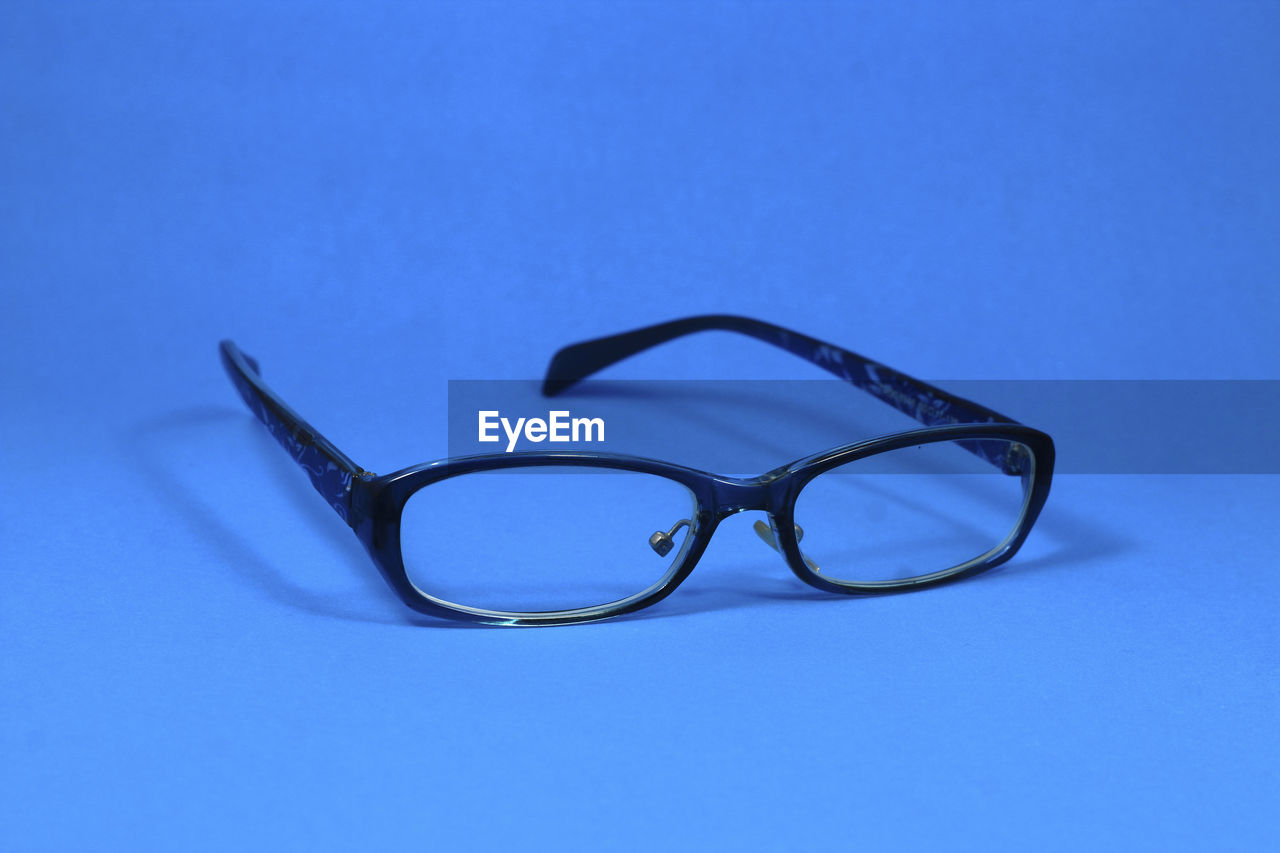 CLOSE-UP OF EYEGLASSES AGAINST BLUE BACKGROUND