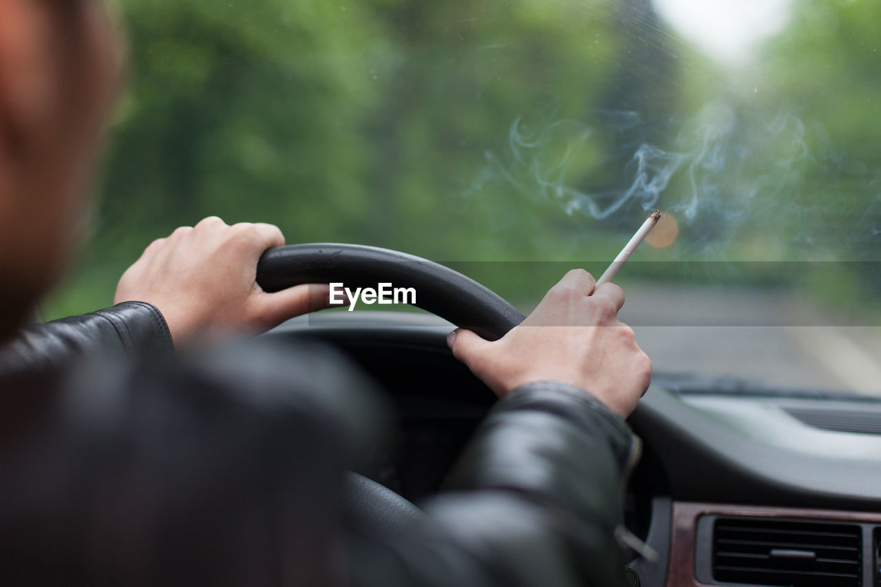 Rear view of mature man holding cigarette while traveling in car