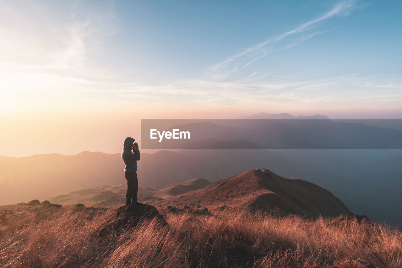 Side view of tourist standing on mountain against sky during sunset