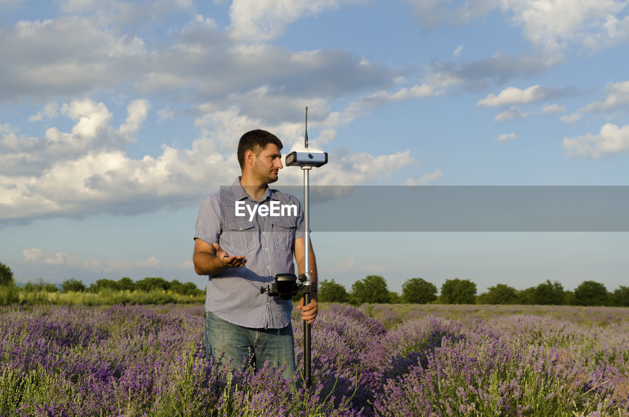 Surveyor with theodolite on lavender field against sky