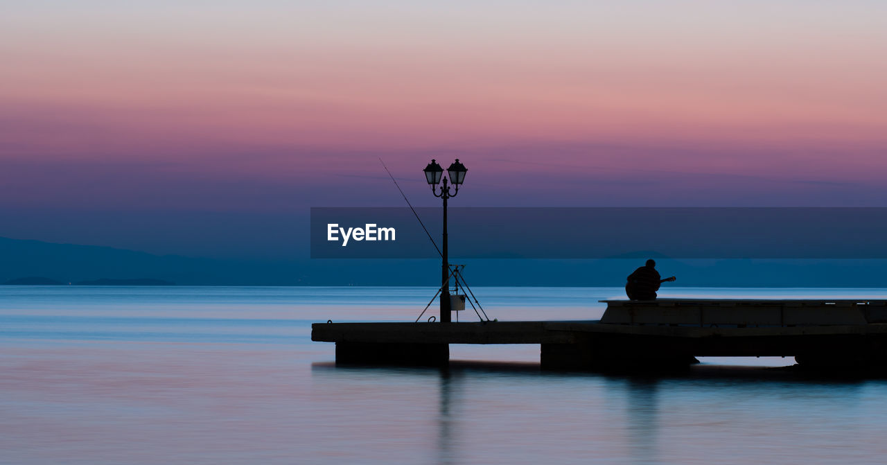 Fisher playing guitar on a pier in greece